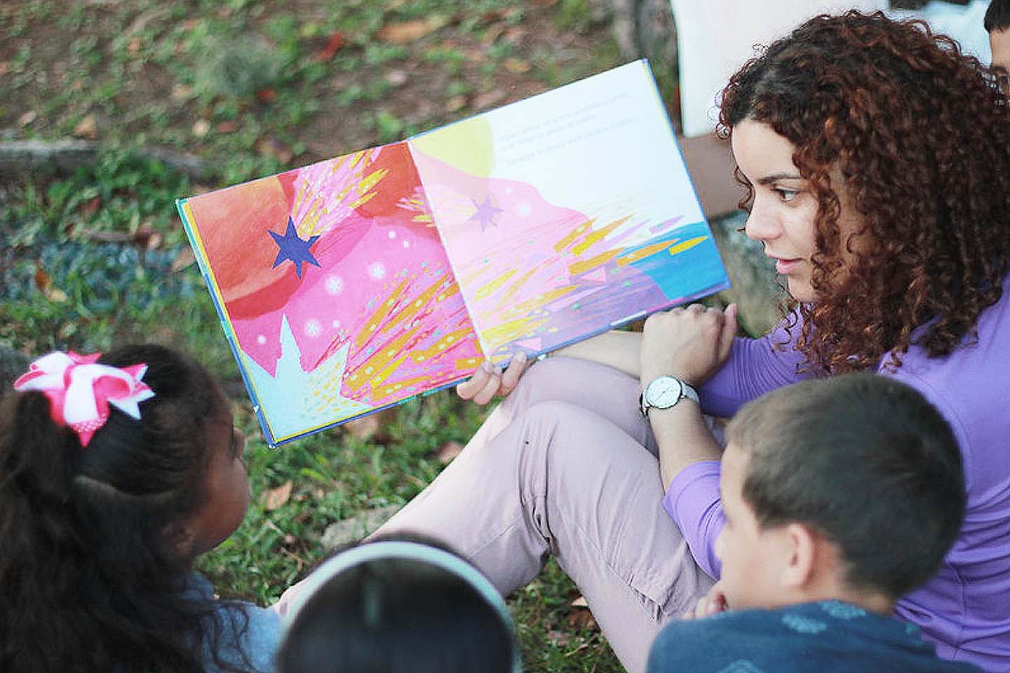 Mujer joven leyendo un cuento a unos niños.